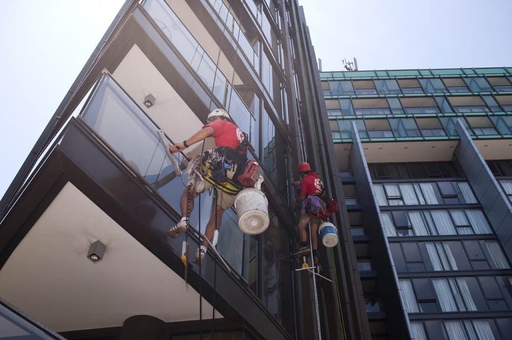 Twee glazenwassers reinigen hangend aan touwen de glazen gevel van een hoog appartementencomplex