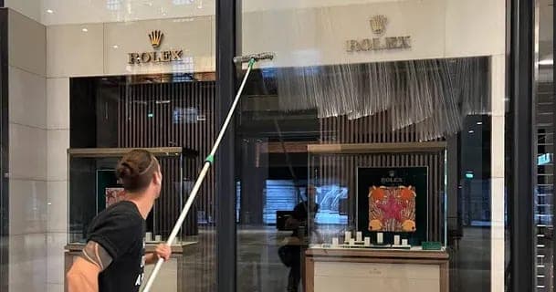 Glazenwasser reinigt de etalageruit van een winkel met een telescoopsteel