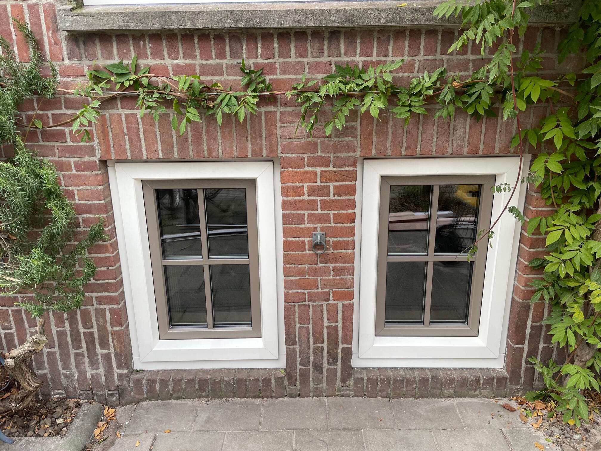 Twee kunststof ramen met roedeverdeling en witte kozijnen in een bakstenen gevel