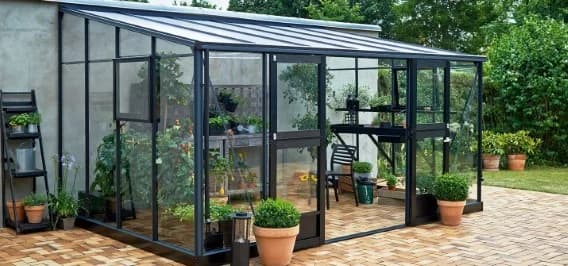 Serre met antracietkleurige kozijnen en glazen dak op een terras in de tuin
