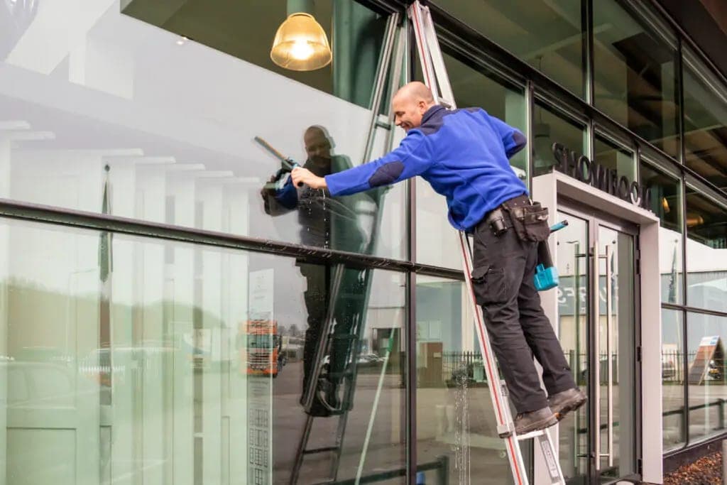 Glazenwasser op een ladder reinigt de glazen pui van een showroom