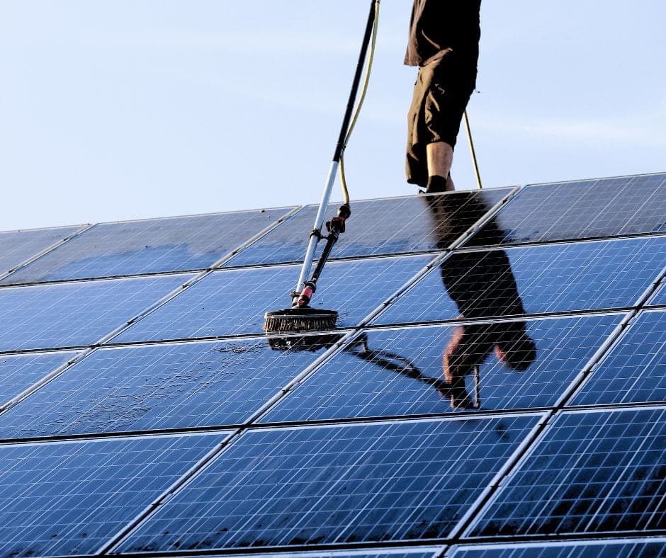 Vakman reinigt zonnepanelen op een schuin dak met een borstel